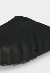 Κοντινό πλάνο ενός μαύρου σανδαλιού Nike slide με υφή και ανάγλυφο λογότυπο Nike swoosh στην κορυφή και στο πλάι.