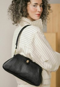 Borsa a mano nera in pelle con superficie strutturata e hardware dorato. Presenta una tracolla sottile e una forma rettangolare ben definita.