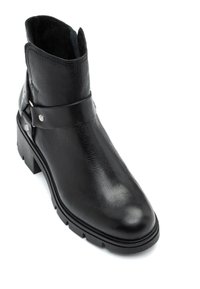 Mustat nahka nilkkurit, joissa on teksturoitu pinta, leveä hihna ja pienet metalliset niitit, tukevalla kumipohjalla.