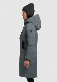 Langer grauer Steppmantel mit Kapuze, der ein Chevron-Steppmuster, seitliche Taschen und ein schwarzes Knopfdetail am Ärmel aufweist.