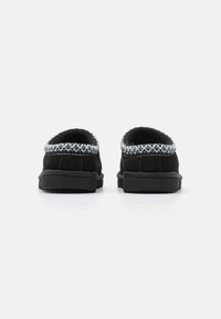 Melni zamš-powered slip-on apavi ar teksturētu, izšūtu apdari. Apaļa aizmugure un plakana gumijas zole, kas rotāta ar zilu un balto dekoratīvo akcentu.