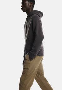 Tumehall kapuutsiga dressipluus, millel on kenguru tasku ja soonikkoes käised, koos beeži värvi pükstega, loodud mugavaks ja vabaks istuvuseks.