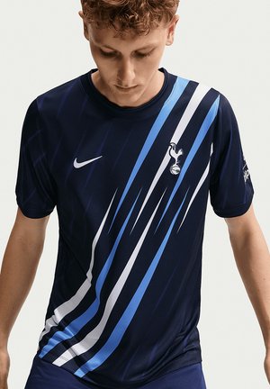 Ung mand iført en mørkeblå Tottenham Hotspur fodboldtrøje med blå og hvide diagonale striber, der kigger nedad.