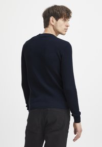 Pulover tricotat texturat de culoare bleumarin, cu mâneci lungi și decolteu rotund, asortat cu blugi negri. Prezintă manșete și tiv cu nervuri.