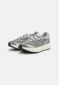 Athletic shoes in grey with mesh and suede materials, featuring white laces, striped accents, and a textured black rubber sole.