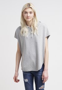 Maglione grigio con cappuccio realizzato in tessuto morbido, caratterizzato da una vestibilità morbida, maniche corte e orlo arrotondato. Abbinato a jeans in denim effetto usurato.