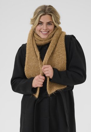 Bufanda de punto color camel con textura de canalé, drapeada alrededor del cuello, contrastada por un abrigo negro con cierre de botones y mangas anchas.