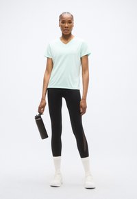 Τυρκουάζ μπλουζάκι με v λαιμόκοψη και κοντά μανίκια, μαύρο κολάν με πλευρικές ανοίγματα, λευκές ασπρόμαυρες κάλτσες αστραγάλου και μαύρο μπουκάλι νερού.