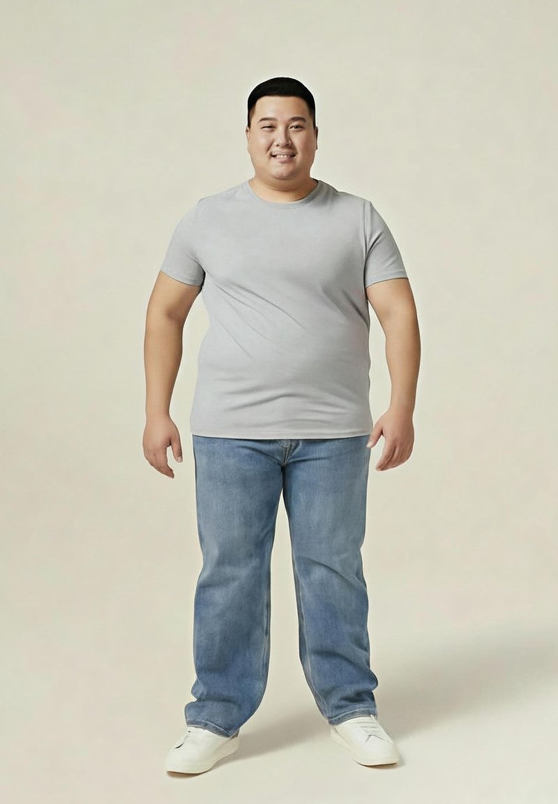 Hombre sonriente de pie, mirando hacia adelante, con una camiseta gris claro, jeans azules y zapatillas blancas, sobre un fondo beige liso.