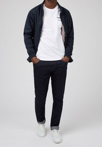 Navy lightweight bomber jacket over a white t-shirt, dark jeans, and white sneakers. Features plaid lining and rolled cuffs.