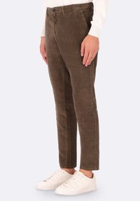 Pantaloni in corduroy marrone con righe verticali, design aderente, tasche frontali, abbinati a sneaker bianche. Tessuto testurizzato, stile a gamba dritta.