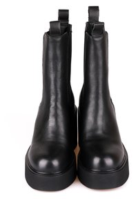 Botas de cuero negras hasta el tobillo con una textura suave, punta redondeada y suela plana y gruesa. Presentan dos tiradores en la parte superior para facilitar su uso.