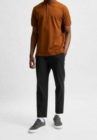 Kort brun polo skjorta med två knappar, svarta skräddarsydda byxor och grå sneakers. Outfiten har en avslappnad passform och mjuka texturer.