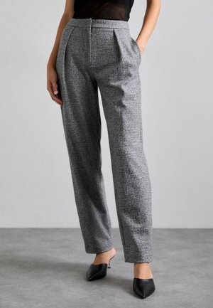 Pantaloni grigi a quadretti con vestibilità su misura, pieghe frontali e tasche laterali, abbinati a décolleté nere a punta. Tessuto dalla texture liscia.