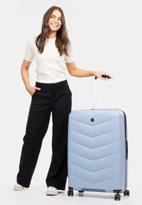 Tvrdý kufr světle modré barvy s vzorem ve tvaru chevron, vybavený teleskopickou rukojetí a černými koly.