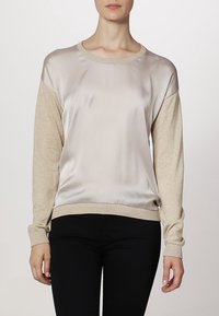 Light beige sweatshirt with shiny satin front and soft knit sleeves. Features a ribbed neckline and cuffs, with a relaxed fit.