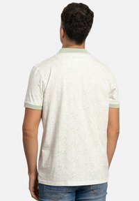 Polo de color verde claro con estampado y mangas cortas, que presenta un cuello y puños acanalados. El material parece tener una textura con un diseño sutil.