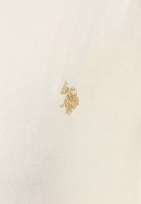 Weißes Baumwoll-T-Shirt mit einem strukturierten, goldfarbenen gestickten Logo eines Pferdes und Reiters auf der linken Seite. Glatte Stoffqualität, lässiges Design.