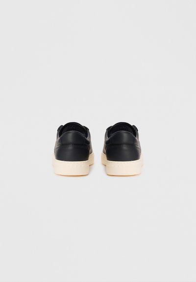 Sneakers negri din piele, cu un design low-top, vârf rotund și talpă din cauciuc de culoare crem. Vederea din spate arată un detaliu subtil de cusătură.