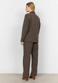 Brun tekstureret blazer og matchende bukser, der har en spids krave og lige ben-design. Båret med brune blokhælede sko.
