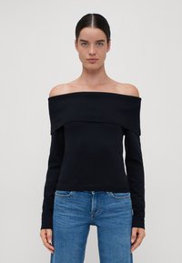 Off-shoulder svart ribbet topp med lange ermer, med en bred halslinning og en tettsittende silhuett, kombinert med blå jeans.