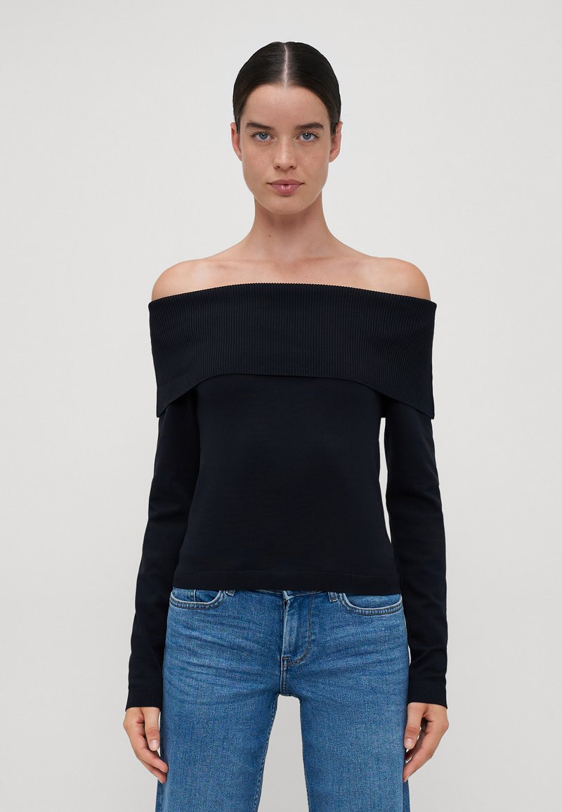 Off-shoulder svart ribbet topp med lange ermer, med en bred halslinning og en tettsittende silhuett, kombinert med blå jeans.