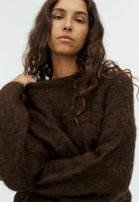 Brown, fuzzy sweater with a loose fit and wide sleeves. Soft texture; features a wide neckline and gathered detail around the arms.