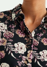 Svart blus med blommönster, utrustad med krage, detaljerade blomsterdesigner i nyanser av rosa, grädde och mörk vinröd, med en mjuk yta.