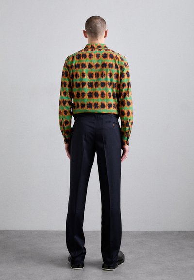Chemise à manches longues imprimée en vert, orange et noir avec col, associée à un pantalon noir formel. Tissu lisse, silhouette ajustée, vue de dos.