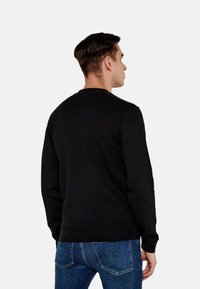 Felpa nera con maniche lunghe, colletto a girocollo e polsini a costine, abbinata a jeans blu, vista di spalle.