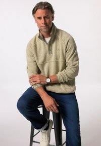 Fleece-pullover i lys grå farve med halvlukket design og olivenfarvede detaljer. Sammen med mørke jeans og hvide sneakers. Glat tekstur, afslappet pasform.