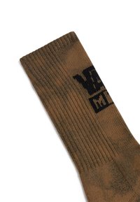 Brun bomuldsstrømpe med ribbet struktur og sort logo-print. Har et lidt mørkere, marmoreret design nær foden.