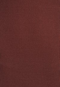 Tessuto a costine di un profondo colore terracotta, che mette in mostra una superficie liscia con linee verticali, creando un aspetto strutturato.