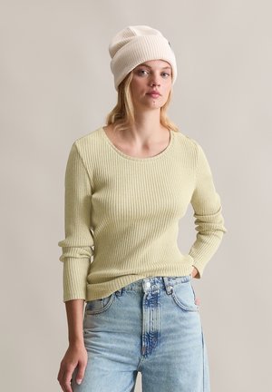 Hellgelbes, geripptes Langarmpullover mit rundem Ausschnitt, kombiniert mit hellblauen, locker sitzenden Jeans und einer cremefarbenen Strickmütze.