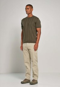 Olijfgroen gebreid sweater met korte mouwen en verticale ribbels, gecombineerd met beige broeken en olijfgroene schoenen. Minimalistisch ontwerp en textuur.