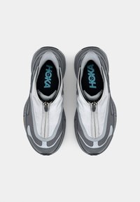 Adidași gri cu un interior texturat, panouri din plasă și un fermoar frontal. Au logo pe glezna și tălpi din cauciuc cu un model.