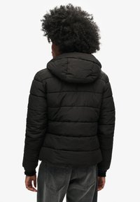 Črn puffer jopič s kapuco, ki ima prešito podlogo, elastične manšete in skrajšan kroj, zasnovan za toploto in udobje.