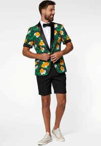 Květinový blazer v zelené, žluté a bílé barvě s černými saténovými klopami, v kombinaci s černými šortkami a bílými teniskami.