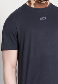 Námorně modré tričko s krátkým rukávem vyrobené z měkké bavlny, s malým bílým logem "MO'PD" na hrudi a kulatým výstřihem.