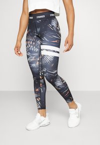 Tight-fittende leggings i mørkt stof med et farverigt abstrakt mønster, der har en hvid stribet talje og en glat tekstur.