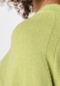 Pull en tricot vert clair avec un col rond et une texture côtelée au niveau du col et des coutures d'épaule. Matériau doux et de poids moyen.