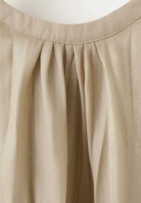 Beige blus med en plisserad design, tillverkad av ett lätt, lätt glansigt tyg. Har en rund halsringning och en mjuk textur.