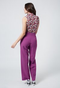 Ärmlös blommig topp med hög krage, kombinerad med högmidjade, vida lila byxor och metalliska silverklackar.