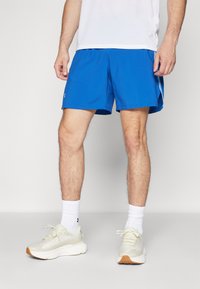 Pantalones cortos deportivos azules de material ligero, con una textura suave y un logotipo. Combinados con calcetines blancos y zapatillas claras.