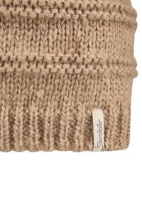 Knit wool hat in light brown, featuring a ribbed texture and a woven label on the side. The design includes alternating stitch patterns.
