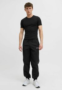 Schwarzes, enges T-Shirt kombiniert mit schwarzen Jogginghosen mit Kordelzug und seitlichen Streifen. Abgerundet mit weißen Sneakers für einen lässigen Look.
