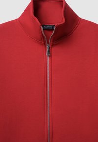 Veste rouge zippée avec un col montant et une fermeture éclair argentée visible, avec une étiquette noire à l'intérieur de l'encolure indiquant "CALLIOPE".