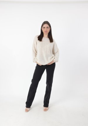 Crème textuur gebreide trui met oversized mouwen, gecombineerd met zwarte rechte broek en lichtgekleurde open teen hakken.