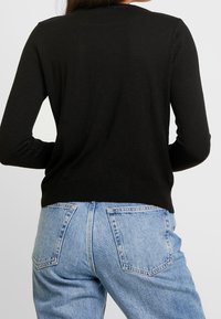 Svart långärmad tröja i mjukt tyg, med ribbad nederkant och mudd, i kombination med ljusblå högmidjade jeans med synliga fickor.