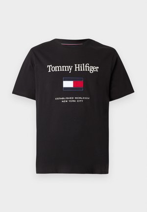Must täielikult must T-särk, millel on valge tikand "Tommy Hilfiger" ja sinine, punane ning valge ristkülikuline logo koos tekstiga "Established 1985."